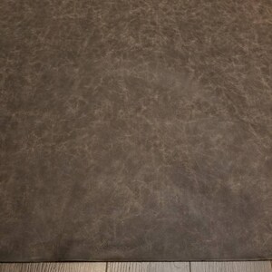 Op de afbeelding: Een close-up van een donkerbruin, getextureerd oppervlak. Het oppervlak heeft een licht ruwe, ongelijke textuur. Het oppervlak is waarschijnlijk gemaakt van leer of een leerachtig materiaal.