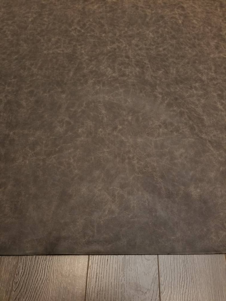 Op de afbeelding: Een close-up van een donkerbruin, getextureerd oppervlak. Het oppervlak heeft een licht ruwe, ongelijke textuur. Het oppervlak is waarschijnlijk gemaakt van leer of een leerachtig materiaal.