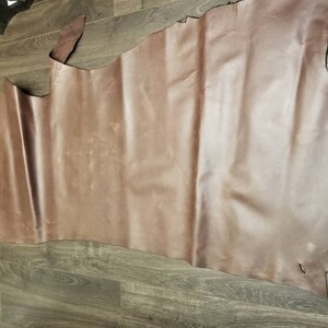 May include: A large piece of brown leather with a smooth, slightly textured surface. The leather is folded in a way that shows its natural grain and color variations.