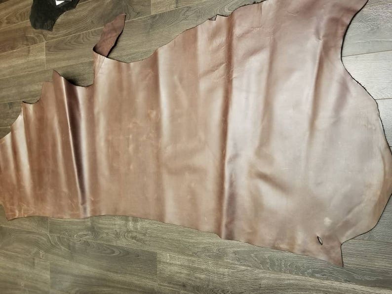 May include: A large piece of brown leather with a smooth, slightly textured surface. The leather is folded in a way that shows its natural grain and color variations.