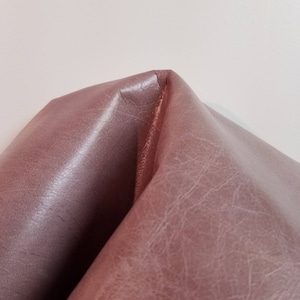 May include: Close-up of a folded piece of mauve leather with a textured surface.
