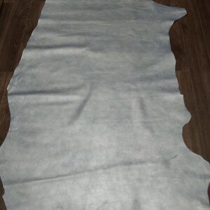 Pode incluir: Uma grande peça de couro azul claro, colocada plana em um piso de madeira.