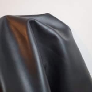 May include: A close-up of a smooth, black leather fabric. The fabric is draped and folded, showing its texture and sheen.