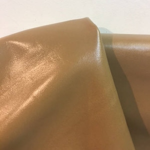 Pode incluir: Close-up de um pedaço de couro marrom com um acabamento liso e brilhante.