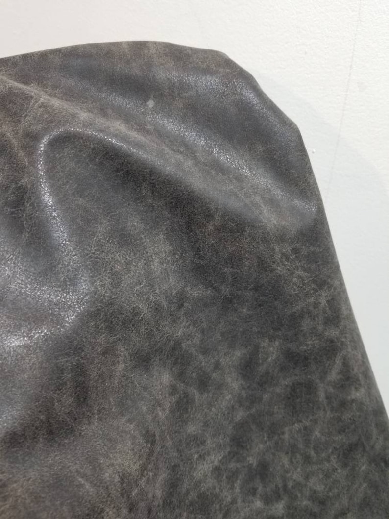 Op de afbeelding: Close-up van een donkergrijze, textuurrijke stof met een licht korrelige uitstraling.