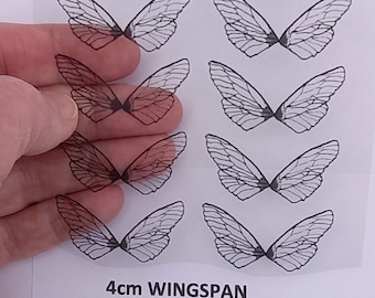 Op de afbeelding: Een vel doorzichtig, transparant vinyl met 12 zwarte vlinder vleugel stickers. Elke sticker heeft een spanwijdte van 4 cm. De tekst "4cm WINGSPAN" is onderaan het vel gedrukt.