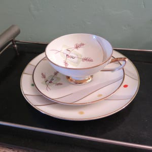 Peut inclure: Un service à thé vintage. La tasse et la soucoupe en porcelaine blanche présentent un bord doré et un motif délicat en forme de blé en rouge et vert. L'ensemble comprend une tasse, une soucoupe et une assiette.