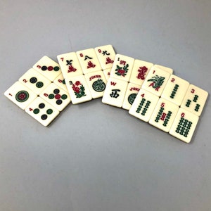 May include: A set of white mahjong tiles with red and green Chinese characters and symbols. The tiles are arranged in a fan shape on a gray surface. The tiles include numbers 1 through 9, the words "Joker", "SPR", "JOKE", and "W", and the Chinese characters for "East", "South", "West", and "North".