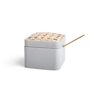 May include: A gray ceramic box with a woven lid and a gold metal stick. The box is square and has a textured surface.