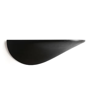 Puede incluir: Una estantería de pared de madera negra con forma de media luna. La estantería es curva y tiene un acabado liso y pulido.
