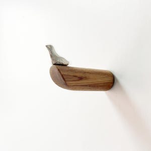 May include: A wooden wall hook with a silver bird perched on top. The hook is curved and has a natural wood grain.