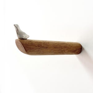 May include: A wooden wall hook with a small silver bird perched on top. The hook is made of natural wood and has a rounded shape.