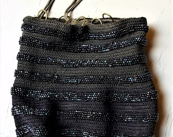 May include: A black beaded bag with a drawstring closure and a long fringe. The bag has a striped pattern and is made of small, iridescent beads.