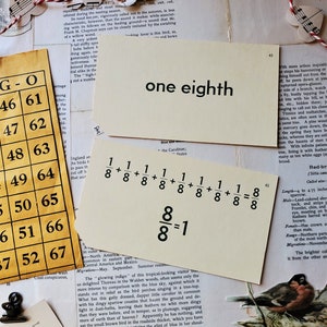 May include: A close-up of a white card with the words "one eighth" written in black ink. The card is surrounded by other pieces of paper with text and images, including a yellow grid with numbers, a red and white string with music notes, and a bird illustration.