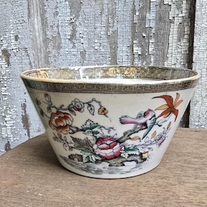 May include: A white ceramic bowl with a floral and bird design. The bowl features a detailed pattern of pink and orange flowers, green leaves, and a bird. The rim has a decorative border.