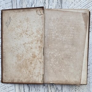 Puede incluir: Un libro antiguo abierto con p&aacute;ginas envejecidas y manchadas. La p&aacute;gina izquierda tiene texto manuscrito en la esquina superior izquierda. La cubierta del libro es de color marr&oacute;n oscuro y las p&aacute;ginas muestran signos de desgaste y edad.