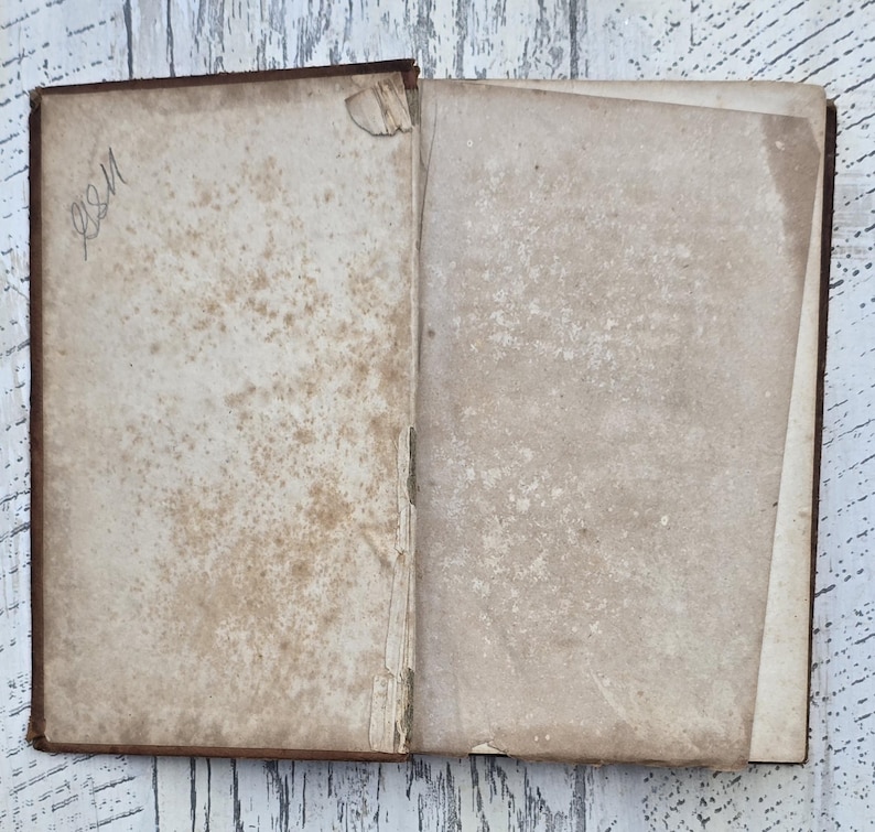 Puede incluir: Un libro antiguo abierto con p&aacute;ginas envejecidas y manchadas. La p&aacute;gina izquierda tiene texto manuscrito en la esquina superior izquierda. La cubierta del libro es de color marr&oacute;n oscuro y las p&aacute;ginas muestran signos de desgaste y edad.