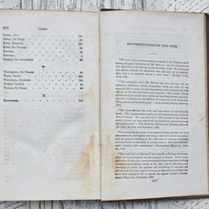 Puede incluir: Libro abierto con p&aacute;ginas envejecidas y amarillentas. La p&aacute;gina izquierda muestra un &iacute;ndice con nombres y n&uacute;meros de p&aacute;gina. La p&aacute;gina derecha contiene texto titulado "Recomendaciones de esta obra". El texto est&aacute; en negro.