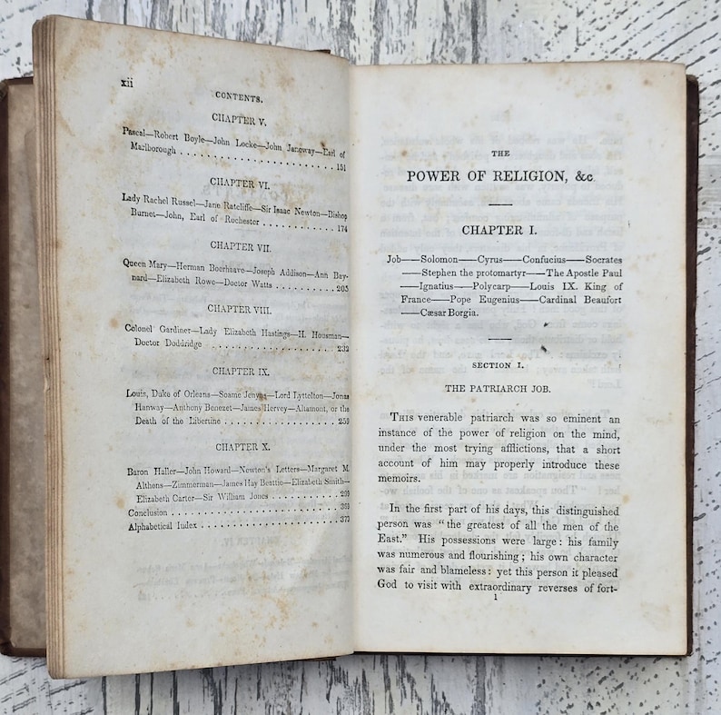 Puede incluir: Libro antiguo abierto con p&aacute;ginas envejecidas y amarillentas. La p&aacute;gina izquierda muestra una tabla de contenidos, mientras que la p&aacute;gina derecha muestra el t&iacute;tulo "The Power of Religion, &c" y el comienzo del Cap&iacute;tulo 1. El libro tiene una cubierta de cuero marr&oacute;n.