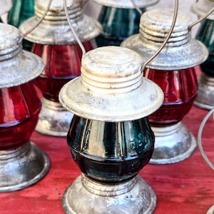 May include: A group of vintage glass lanterns with metal frames and handles. The lanterns have red and green glass panels and are arranged on a red surface.