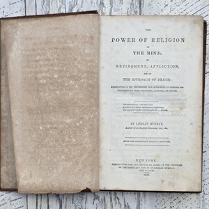 Puede incluir: Un libro antiguo abierto con una cubierta de cuero marr&oacute;n y p&aacute;ginas amarillentas envejecidas. El t&iacute;tulo, "THE POWER OF RELIGION", es visible, junto con otro texto. El libro es de Nueva York, 1830.