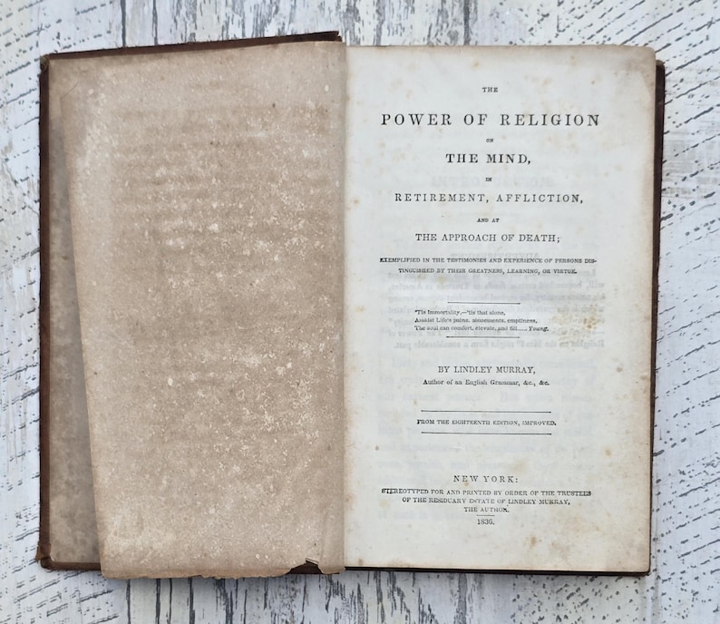 Puede incluir: Un libro antiguo abierto con una cubierta de cuero marr&oacute;n y p&aacute;ginas amarillentas envejecidas. El t&iacute;tulo, "THE POWER OF RELIGION", es visible, junto con otro texto. El libro es de Nueva York, 1830.