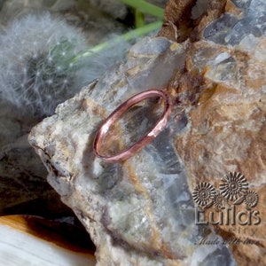 Könnte beinhalten: Ein gehämmerter Kupferring auf einem Gesteinshintergrund. Der Ring ist ein schlichtes Band mit einer glatten, polierten Oberfläche. Der Ring ist eine beliebte Wahl für minimalistischen Schmuck.