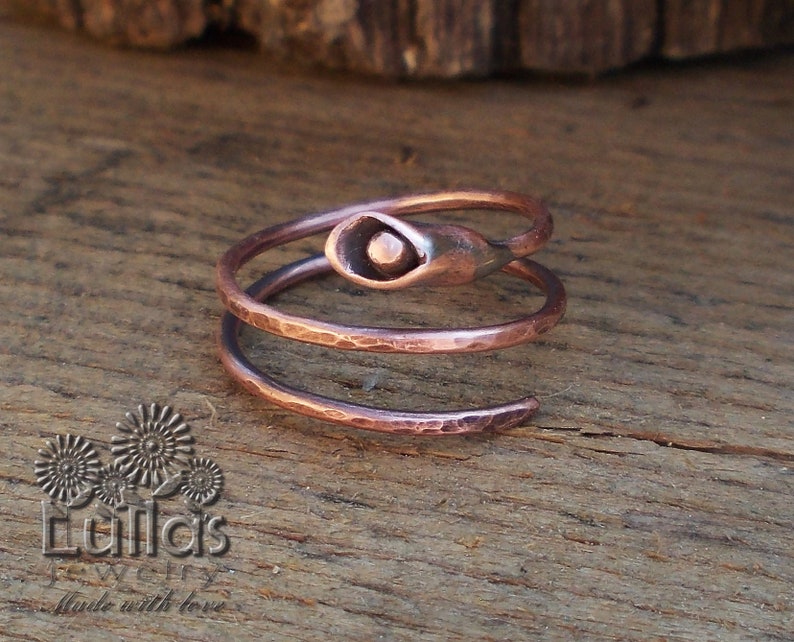 May include: A copper ring with a hammered finish and a swirl design. The ring has a small, round, copper accent on the top.