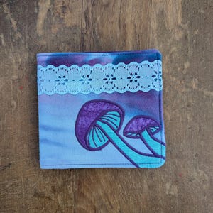 May include: A blue fabric wallet with a purple and blue mushroom design and a white lace trim.