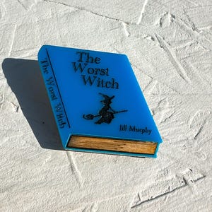 May include: A blue book-shaped resin ornament with the title "The Worst Witch" and the author "Jill Murphy" printed on the front.