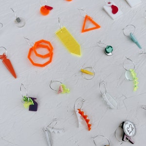 May include: A collection of colorful earrings featuring various shapes and designs, including geometric shapes, a carrot, a leaf, and a zig-zag pattern. The earrings are made of acrylic and are perfect for adding a pop of color to any outfit.