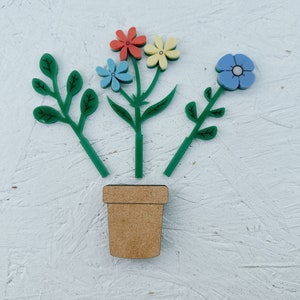 May include: A wooden flower pot with four colorful flowers and green stems. The flowers are red, yellow, blue, and light blue.