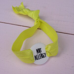 May include: A yellow elastic bracelet with a white button that says "NUT ALLERGY".
