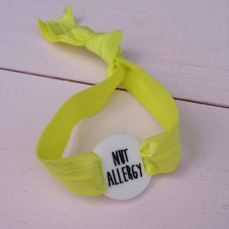 May include: A yellow elastic bracelet with a white button that says "NUT ALLERGY".