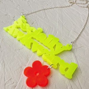 May include: A neon yellow necklace with the words "Absolutely Awkward" and a bright red flower charm.