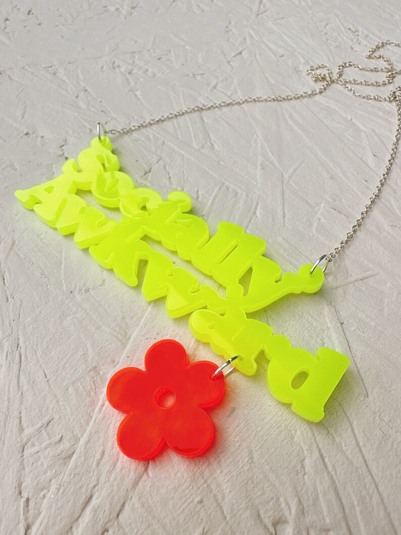 May include: A neon yellow necklace with the words "Absolutely Awkward" and a bright red flower charm.