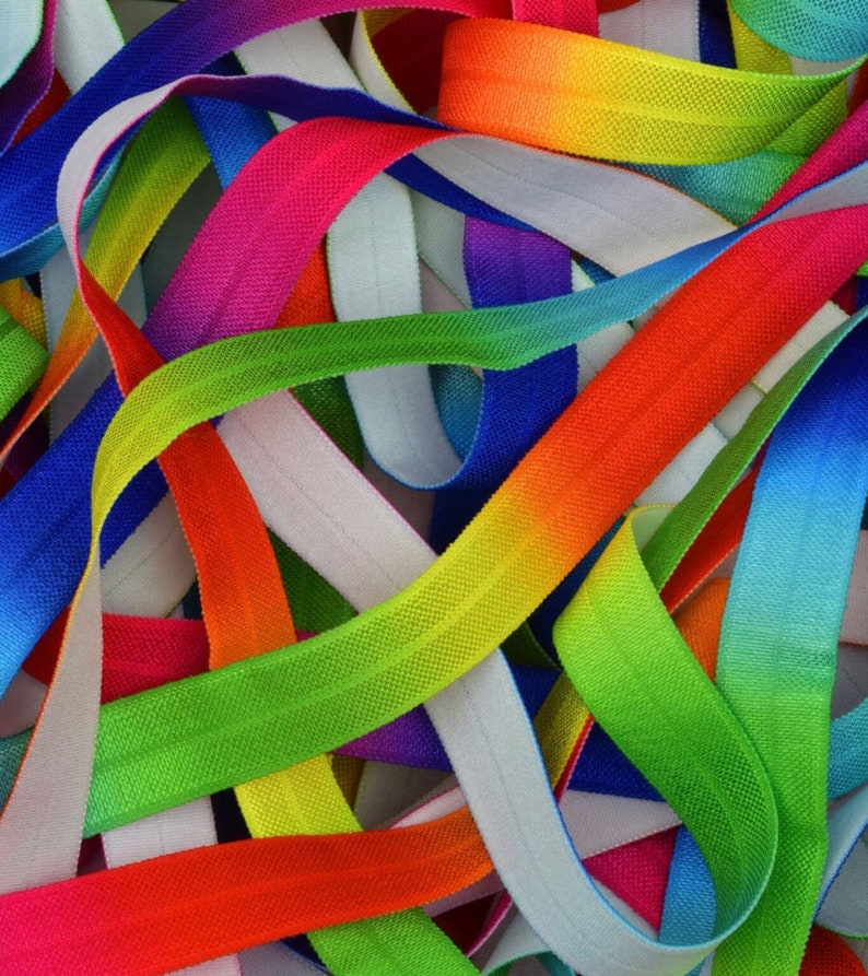 May include: A close-up of a pile of colorful elastic bands with a rainbow ombre effect. The bands are made of a soft, stretchy material and are perfect for crafts, hair ties, or other projects.