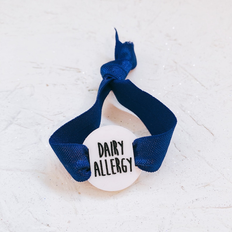 May include: A blue fabric wristband with a white round tag that says "Dairy Allergy".