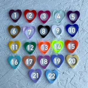 May include: Twenty-two heart-shaped resin blanks in various colors, numbered 1 through 22. The blanks are arranged in rows, with the first row containing five blanks, the second row containing six blanks, the third row containing five blanks, and the final row containing two blanks.