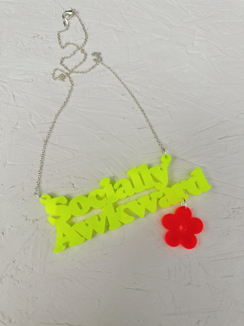 May include: A neon yellow necklace with the words "Socially Awkward" and a red flower charm.