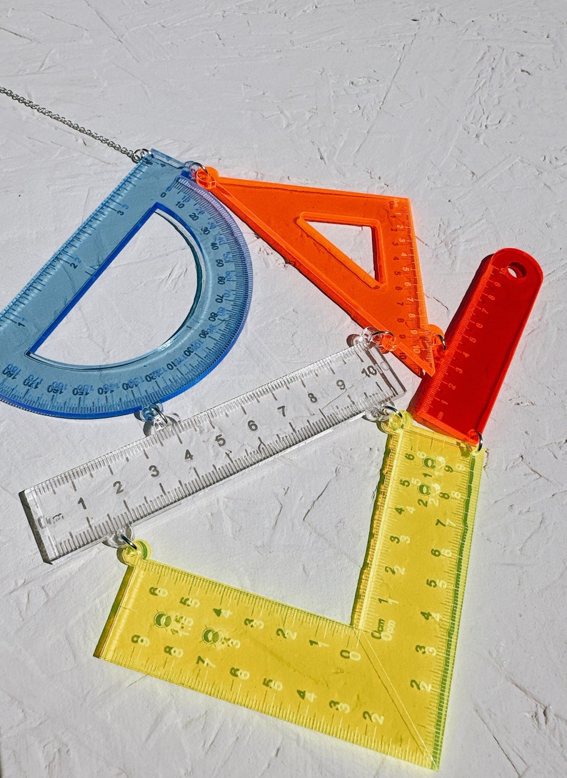 以下が含まれることがあります： 分度器、三角形、定規など、カラフルな幾何学定規のセット。定規は銀色のチェーンでつながっています。