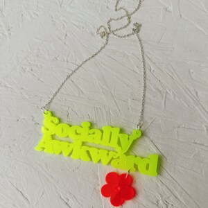 May include: A neon yellow necklace with the words "Socially Awkward" and a red flower charm.