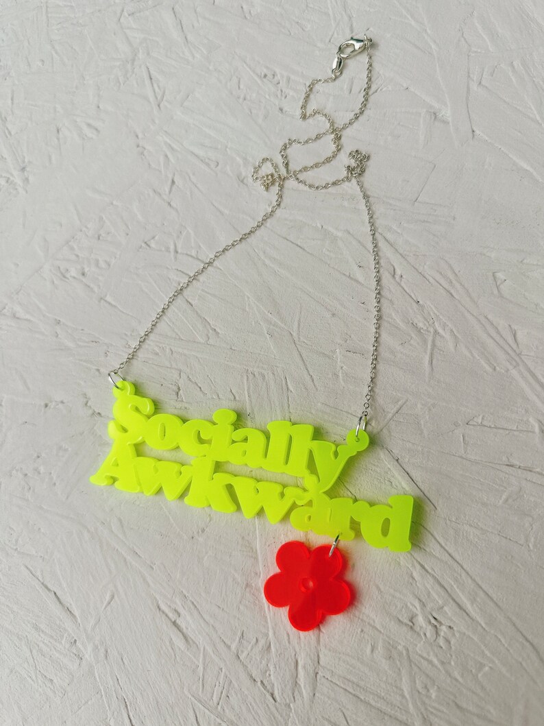 May include: A neon yellow necklace with the words "Socially Awkward" and a red flower charm.