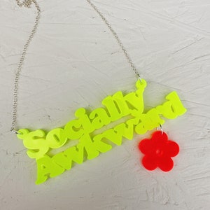 May include: A neon yellow necklace with the words "Socially Awkward" and a red flower charm.