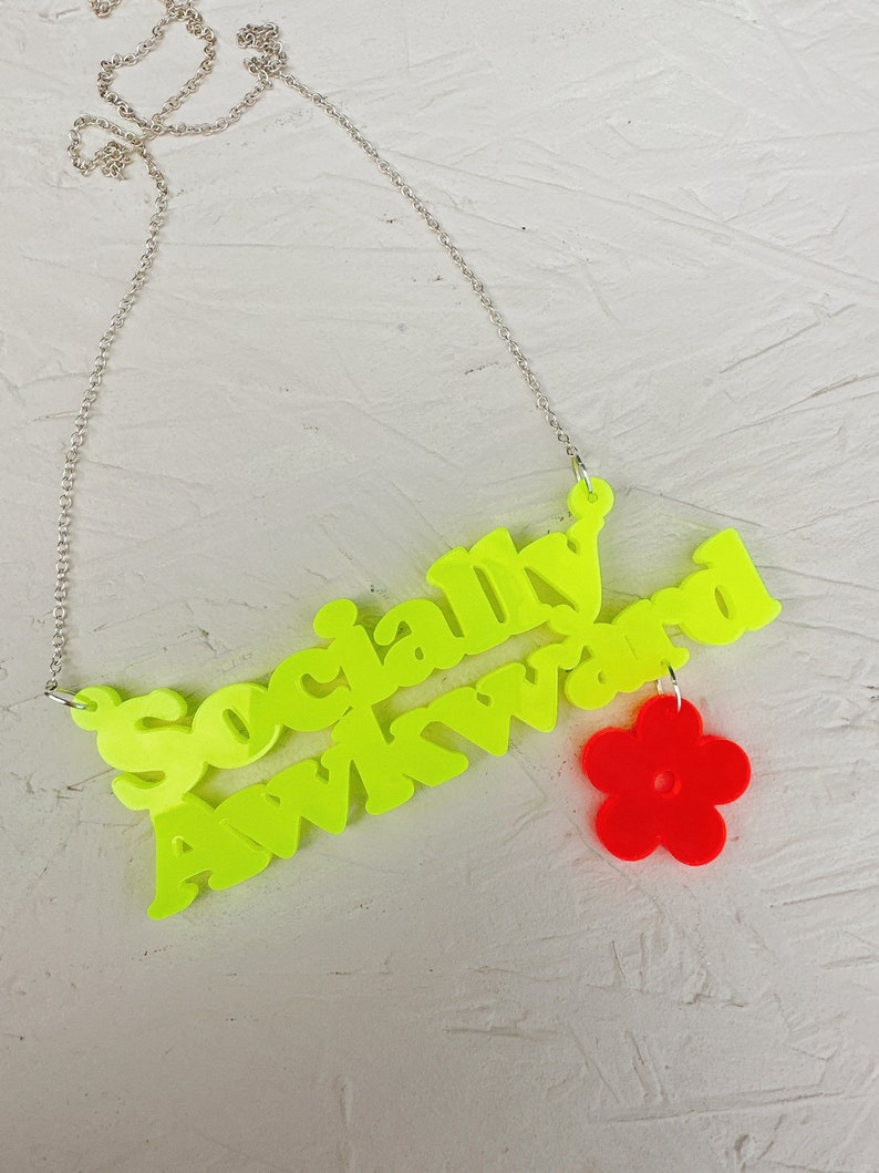 May include: A neon yellow necklace with the words "Socially Awkward" and a red flower charm.