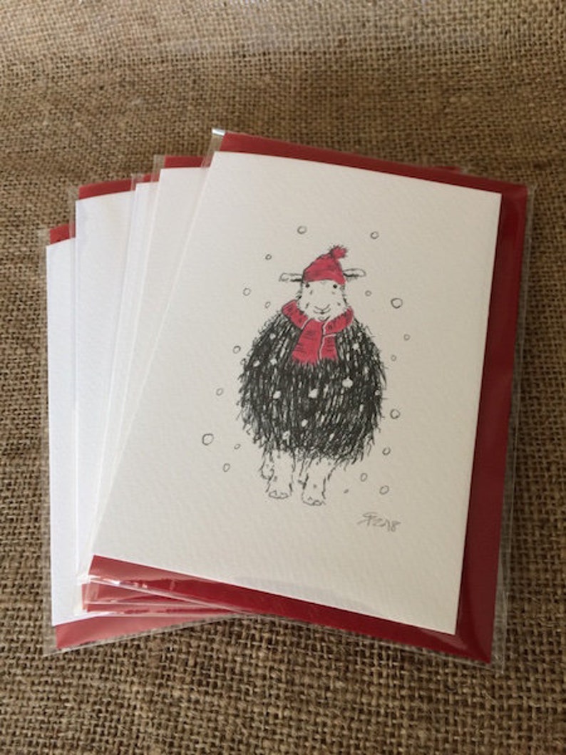 May include: A pack of five blank greeting cards with red envelopes. The card features a black and white illustration of a sheep wearing a red hat and scarf in a snowy scene. The card is signed "AF 2018".