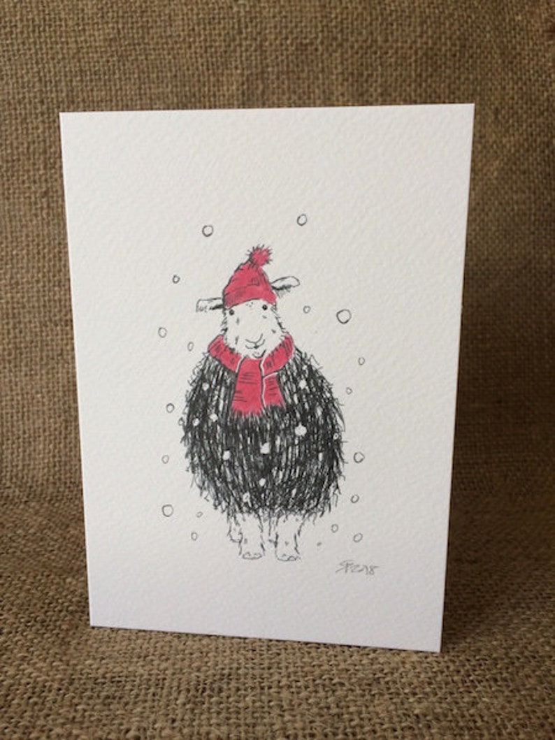 May include: A black and white illustration of a sheep wearing a red hat and scarf in a snowy scene. The sheep is looking to the right and has a happy expression. The illustration is on a white card.