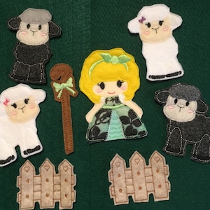 Puede incluir: Un conjunto de figuras de fieltro que incluye un personaje con cabello amarillo y vestido verde, un cayado de pastor marr&oacute;n con un lazo verde, dos ovejas blancas con lazos rosas, dos ovejas negras y dos vallas de estacas beige con corazones.