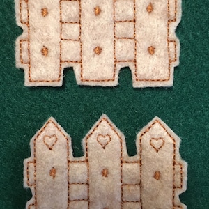 Puede incluir: Dos recortes de valla id&eacute;nticos de fieltro color blanco roto con tres estacas verticales de punta. Cada estaca est&aacute; decorada con el contorno de un coraz&oacute;n bordado y dos peque&ntilde;os puntos de costura marrones, todo perfilado con hilo marr&oacute;n.