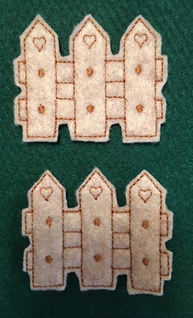 Puede incluir: Dos recortes de valla id&eacute;nticos de fieltro color blanco roto con tres estacas verticales de punta. Cada estaca est&aacute; decorada con el contorno de un coraz&oacute;n bordado y dos peque&ntilde;os puntos de costura marrones, todo perfilado con hilo marr&oacute;n.
